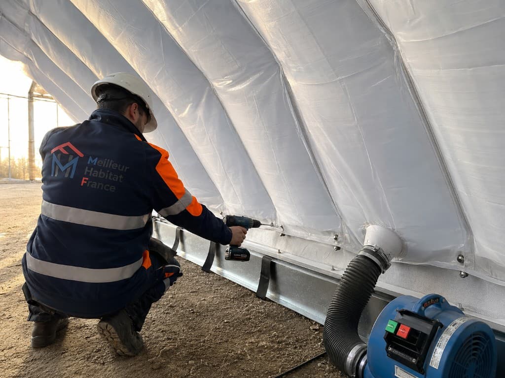 Technicien MHF en gilet Meilleur Habitat de France pose une vis sur le rail d’une double paroi gonflable de serre, avec souffleur d’air connecté.